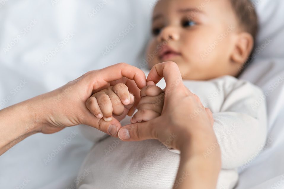 Black mother holding baby's hands in heart shape